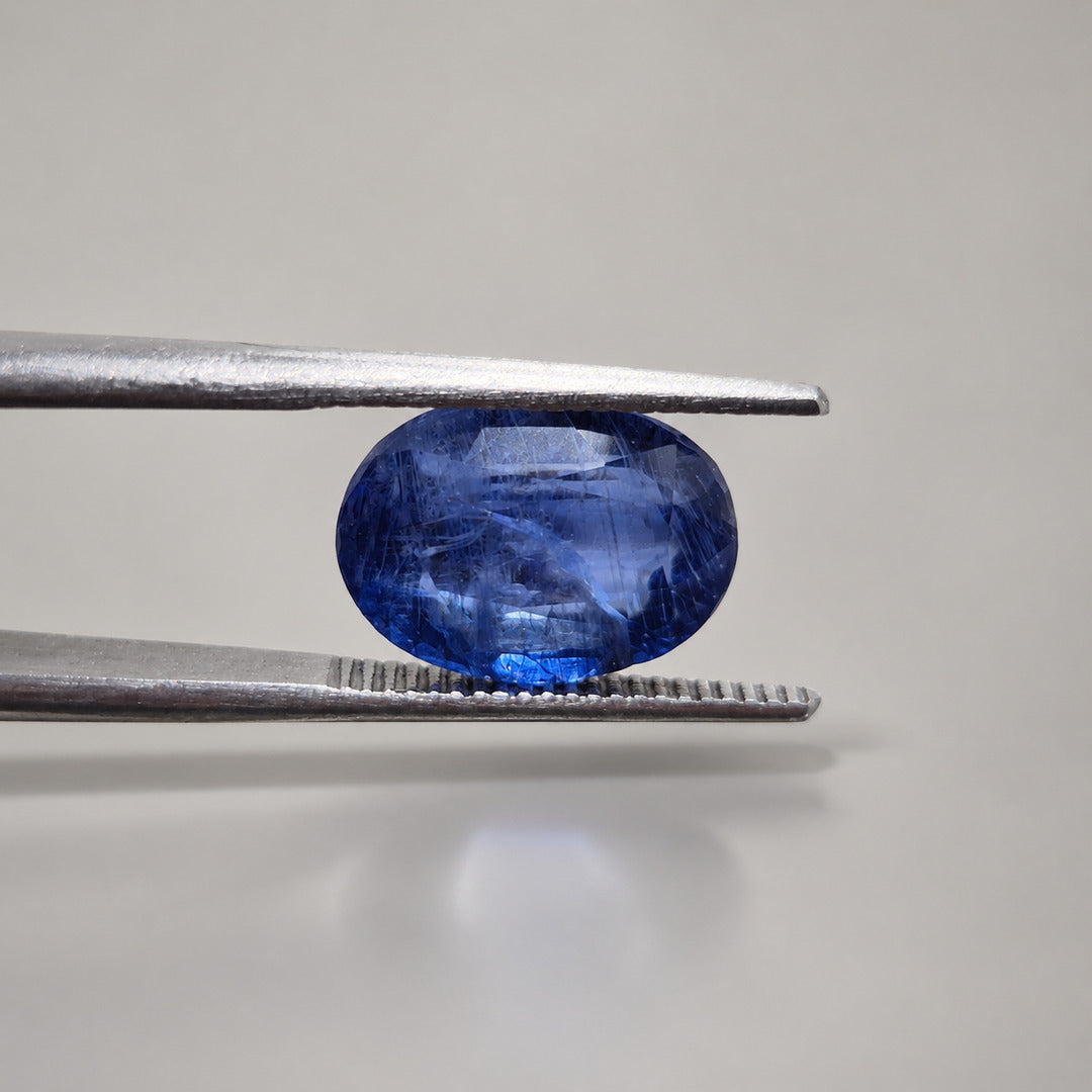Blue sapphire oval gemstone held in gemmological tweezers to show depth and profile