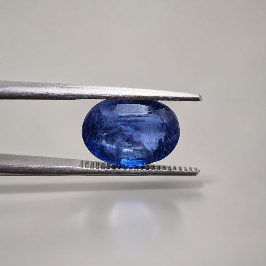 Blue sapphire oval gemstone held in gemmological tweezers to show depth and profile