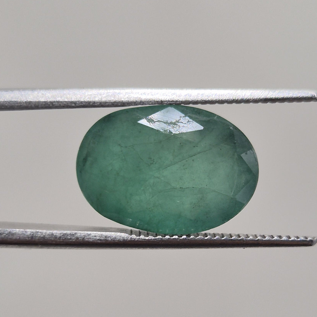 Emerald oval cut gemstone held in tweezers, showing its soft green colour and faceted crown