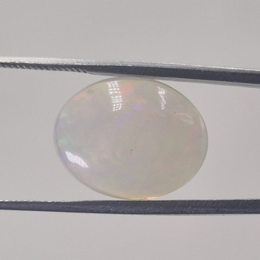 Opal oval cabochon gemstone with a milky white body and faint spectral play of colour